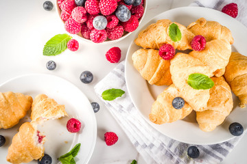 Sweet summer dessert, homemade baked mini croissants with berry jam, served with tea, fresh raspberries, blueberries and mint. On a white marble table, copy space top view