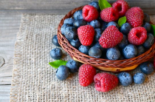 Freshly picked organic raspberries and blueberries in a basket on old wooden background.Blueberry and raspberry.
Healthy eating,summer fruits or diet concept.Selective focus.