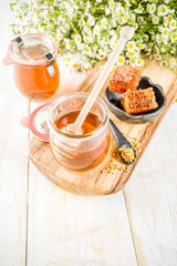 Organic floral honey, in jars, with pollen and honey combs, on a white wooden table, with wildflowers, copy space top view