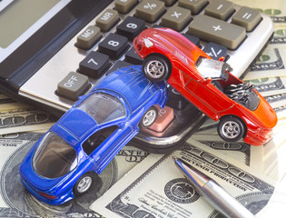 concept of car accident loss and damage. Calculator on the heap of us hundred dollars. two model cars above calculator.Pen lying on dollar bill.