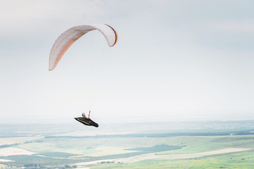White orange paraglide with a paraglider in a cocoon against the background of fields of the sky...