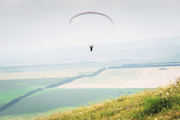 White orange paraglide with a paraglider in a cocoon against the background of fields of the sky and clouds. Paragliding Sports