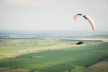 White orange paraglide with a paraglider in a cocoon against the background of fields of the sky...