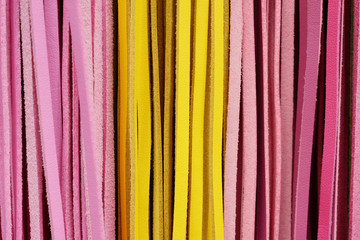 Cutout texture closeup on multiple pink and yellow multicolored leather straps.