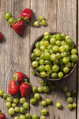 ripe gooseberry in a plate and strawberries in a garden on a table