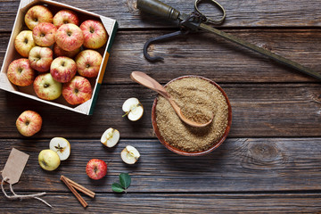 Fresh juicy apples in wooden box, steelyard, brown sugar and cinnamon sticks – ingredients for homemade apple jam. Close-up, top view, space for your text on wooden background in vintage stile.