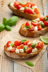 Bruschetta with tomatoes, mozzarella cheese and basil on a old rustic table. Traditional italian appetizer or snack, antipasto