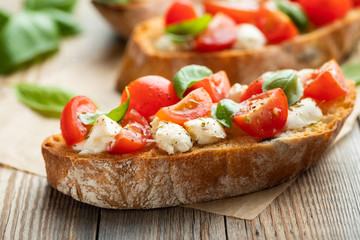 Bruschetta with tomatoes, mozzarella cheese and basil on a old rustic table. Traditional italian appetizer or snack, antipasto