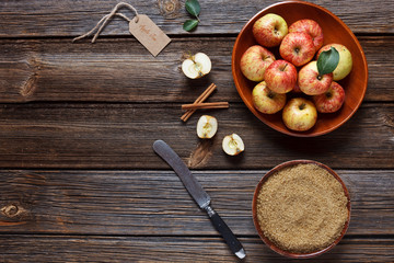 Fresh juicy apples in wooden bowl, brown sugar and cinnamon sticks – ingredients for homemade apple jam. Close-up, top view, space for your text on wooden background in vintage stile.