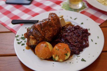 Bayrisches Essen mit Schweinshaxen, Semmelknödel und Rotkraut auf rot karierter Tischdecke