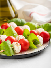 Caprese salad - skewer with tomato, mozzarella and basil, italian food and healthy vegetarian diet concept on a light background
