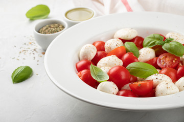 White plate of classic delicious caprese salad with ripe tomatoes, mozzarella and fresh basil leaves on gray background. Italian food. The concept of a healthy vegetarian diet