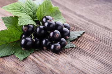 Fresh ripe black currant with original leaves on old wooden background close-up