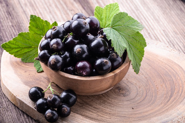 Fresh ripe black currant in wooden bowl with original leaves on rustic old background
