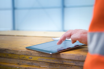 Male engineer using digital tablet at construction site, only hand and part of body in orange...