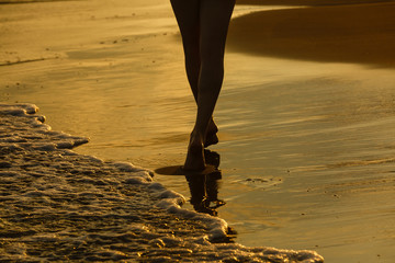 Closeup of woman's feet walking on the beach during a golden sunset.