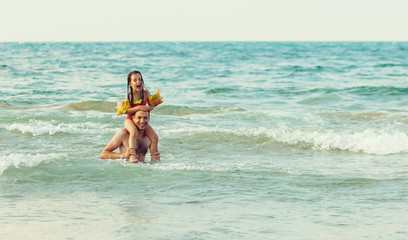 A man with a child, having fun swimming in the sea, the father rolls his daughter on his back, they have fun in the daytime