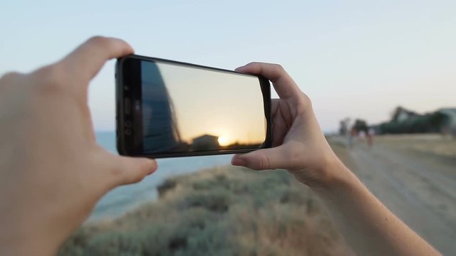 Woman photographs and makes a video the sea landscape on the phone (smartphone).