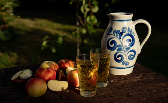 Traditional apple wine in the city of Frankfurt in Hesse. A jug of wine is on an old wooden table in the garden, around it are apples