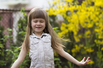 Portrait of a pretty little long-haired blond preschool girl in sleeveless white dress smiling...