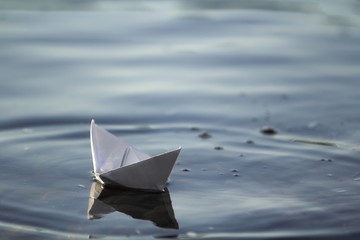 Close-up of simple small white origami paper boat floating quietly in blue clear river or sea water under bright summer sky. Freedom, dreams and fantasies concept, copyspace background. © bilanol
