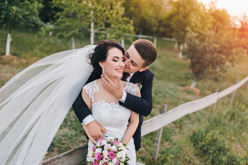 Beautiful newlyweds hugging a background of green grass and nature. Wedding portrait close-up of smiling bride and groom with long veil.