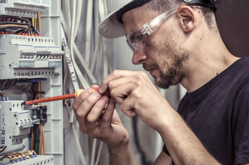a male electrician works in a switchboard with an electrical connecting cable