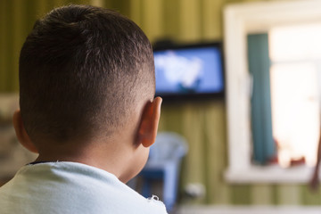 A young boy is watching a television screen with his back for a tv effect on children or a...