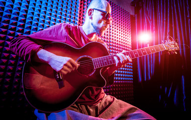 Young man playing on the acoustic guitar in sound recording studio.