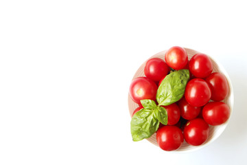 White ceramic bowl full of freshly picked small ripe organic cherry tomatoes with basil leaves, isolated on white background. Clean eating concept. Local produce. Copy space, close up, top view.