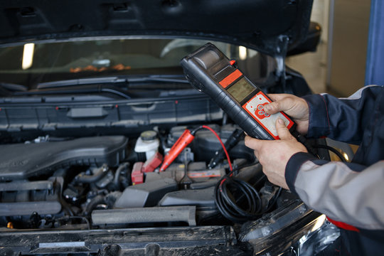 auto mechanic uses multimeter voltmeter to check voltage level in car battery.