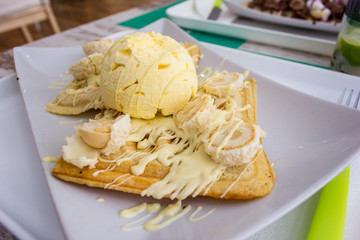 Belgian waffles with melted white chocolate, vanilla ice cream and coconut flakes on light wooden background.