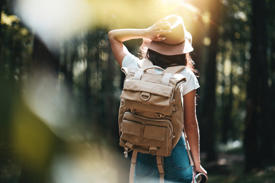 Young Woman Traveler With Backpack Walking Among Trees At Forest In Sunset