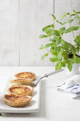 Four individual mini quiches in a row on a white rectangular plate