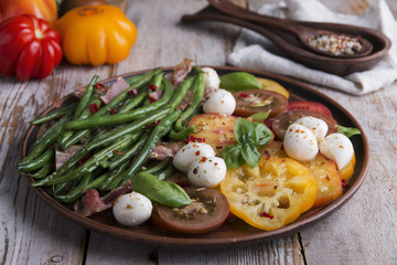 green bean fried with bacon tomato and mozzarella cheese on a plate