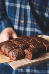 Freshly baked brownies on wooden serving board. Hands holding tray with brownies