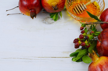 Holiday border on white washed rustic wooden table for Jewish holidays of Rosh Hashana or Yom Kipper. Includes apple, pomegranate and honey with honey dipper. Copy space