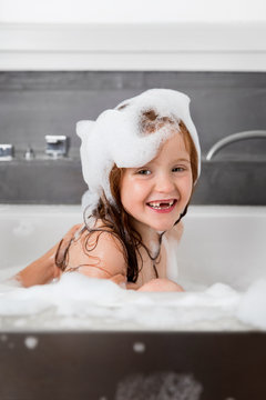 Young girl with missing teeth smiling in soapy bubble bath