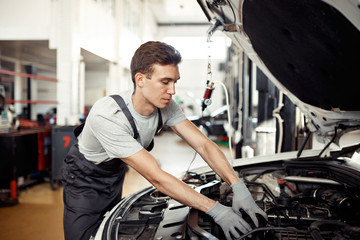 Fototapeta na wymiar A good-loking young mechanic is reparing a vehicle at his work