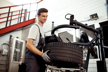 A good-looking mechanic is repairing a wheel at a car service
