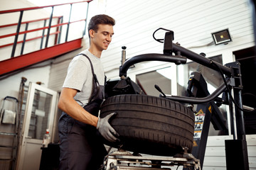 Fototapeta na wymiar Car repair service and maintenance: a young man is at work repairing a tire