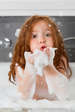 Redhead girl in soapy bubble bath blowing suds