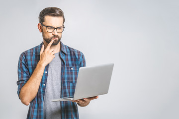 Confident business expert. Confident thoughtful young handsome man in shirt holding laptop and while standing against grey background