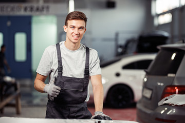 A young happy and smiling mechanic is standing near cars at a car service