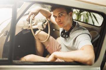 An attractive young man is sitting in a vintage car