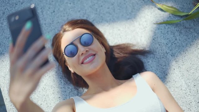 Attractive young girl making selfie and lying in the park