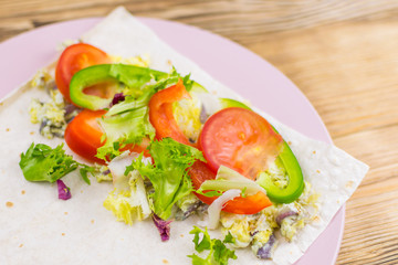 Preparation of a roll of pita bread and fresh vegetables on a wooden background. The concept of healthy eating.