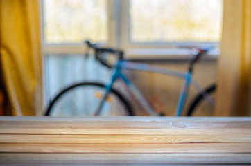 Empty Wooden Table in Front of Blurred Background of Living Room with a Blue Bicycle Near the Window. Mock Up for Display of Product. Blank for Your Layout