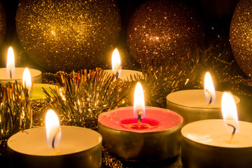 Burning candles surrounded by shiny balls and decor on a dark background.