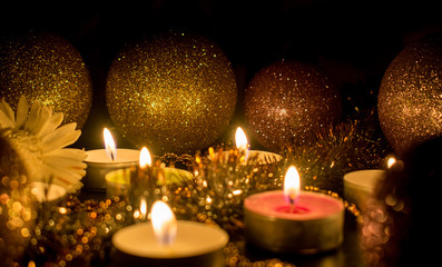 Burning candles surrounded by shiny balls and decor on a dark background.